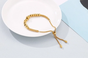Detail of adjustable gold beaded bracelet featuring a polished slide clasp and drop pendants