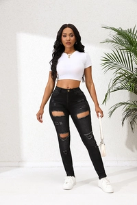 Détail d'un jean skinny noir déchiré à taille haute avec un crop top blanc ajusté
