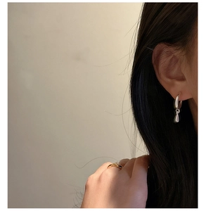 Detailed view of silver water drop earrings and a thin gold pearl ring on a model