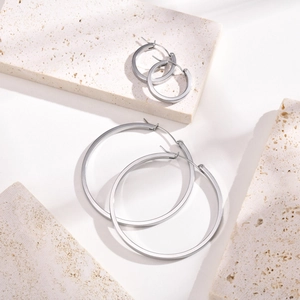 Detailed view of two pairs of polished silver hoop earrings on a stone display