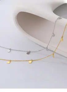 Detail of silver and gold minimalist necklaces with flat round disc charms on white ceramic