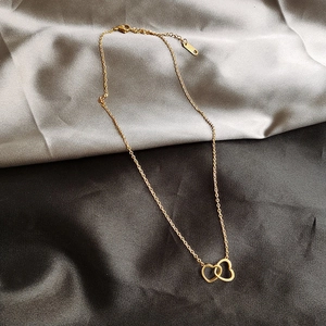 Detailed close-up of double-heart intertwined pendant on a gold necklace with lobster clasp