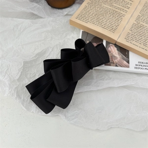 Close-up of a large black satin bow banana clip on an aesthetic minimalist background