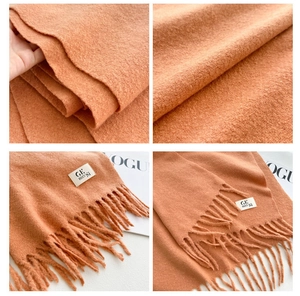 Detail of soft thick orange scarf showing plush wool texture and delicate fringe tassels