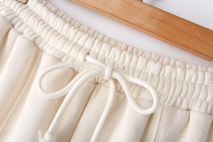 Detail view of cream high-waisted joggers featuring an elastic drawstring waist and soft knit