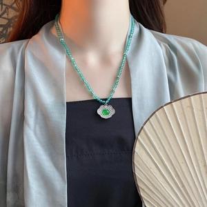 Detail of emerald green beaded necklace with floral pendant on a silk fabric background