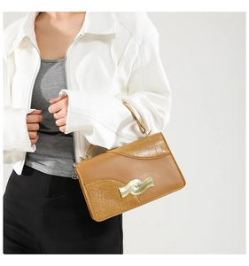 Detail of brown PU leather handbag featuring faux crocodile texture and golden wavy buckle