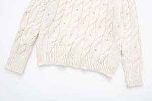Detailaufnahme von weißem Strickpullover mit Zopfmuster und silbernen Strasssteinen