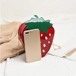 Macro shot of red strawberry shaped crossbody bag with gold chain and phone for scale