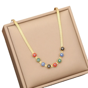 Gold flat snake chain necklace with colorful evil eye charms on a beige display box