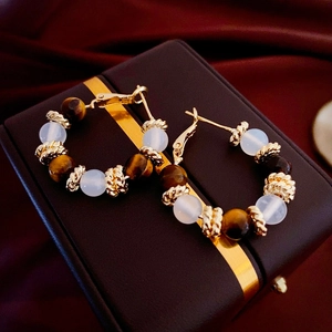 Detailed shot of golden hoop earrings with tiger eye beads and frosted white stones