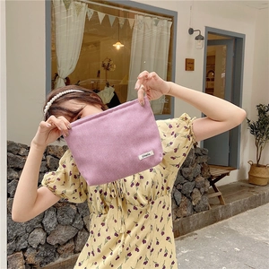 Detailed close-up of a lilac corduroy makeup bag held by a model in a cafe setting
