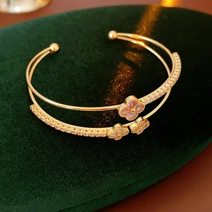 Close-up of double-layer gold bangle with cubic zirconia clover charms and open design