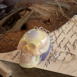 Iridescent skelet sleutelhanger van hars met zilveren ketting op een vintage achtergrond