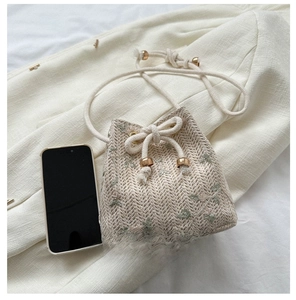 Détail d'un mini sac seau en paille avec broderie florale et fermeture dorée à cordon