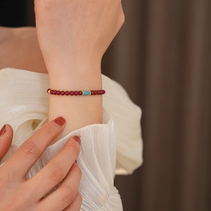 Detail of cinnabar bead bracelet with turquoise barrel bead and gold spacers on wrist