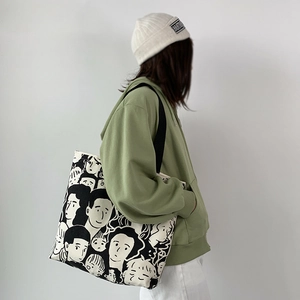 Black canvas tote bag with portrait print worn over shoulder by a model in casual style