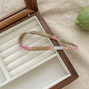 U-shaped acetate hair pin in pink and green gradient placed in a velvet jewelry box
