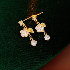 Close-up of gold flower earrings with white petals and zircons on green velvet