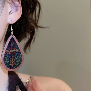 Close-up of teardrop wooden earring with cross print and stained glass pattern on model