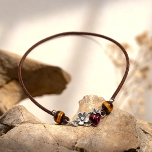 Macro shot of tiger eye beads with strawberry and flower charms on a woven bracelet