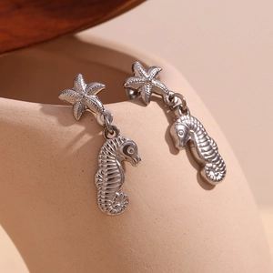 Macro shot of silver seahorse and starfish pendant earrings on a ceramic pot rim