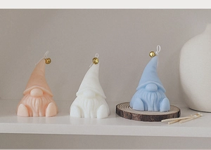 Detailed view of three pastel gnome candles with golden bells on a minimal wooden tray