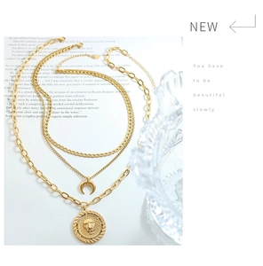 Detail of layered 18K gold-plated necklaces with lion coin and crescent moon pendants