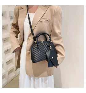 Détail du sac bandoulière noir matelassé en V avec breloque sur blazer kaki