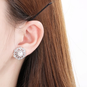 Macro detail of silver flower earring with pearl and zircon inlay on model's ear