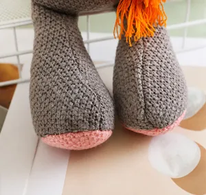 Vue détaillée des pieds de la peluche tricotée grise avec semelles roses et pompons