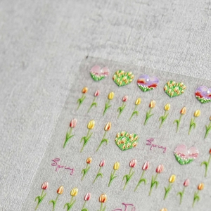 Macro shot of embossed tulip nail art stickers with heart patterns and spring lettering