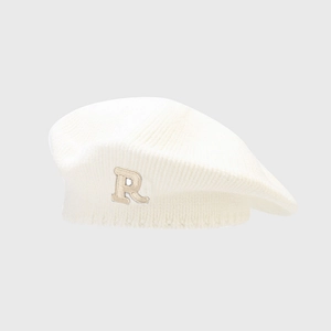 Detailed view of cream knit beret showing fine texture and beige 'R' letter patch