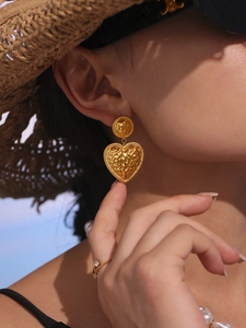 Detailed view of heart-shaped gold-plated earrings with a hammered texture on a model