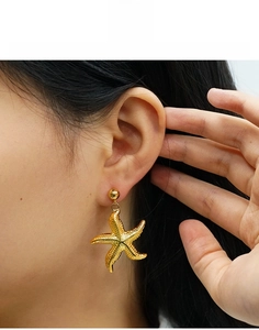 Close-up of golden starfish earrings in titanium steel with detailed metallic texture