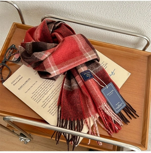 Detailed view of red-brown plaid scarf with fringe on wooden tray with cozy props