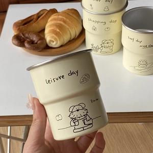 Close-up of a hand holding an off-white stainless steel dog doodle camping mug outdoors