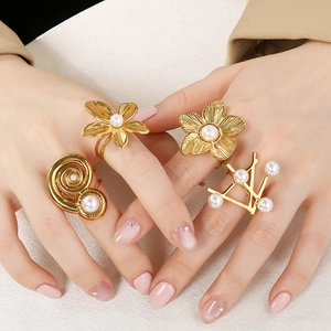 Nahaufnahme von goldenen Edelstahlringen mit Perlen und Blumen an den Händen des Models