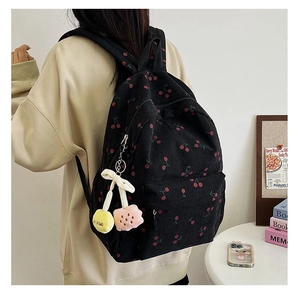 Close-up of black corduroy backpack with cherry pattern and cute plush pendant charm