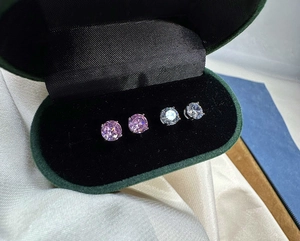 Detailed view of four-prong round-cut purple and clear stud earrings in a velvet gift box