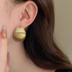 Primo piano di un orecchino a perno ovale in oro spazzolato dallo stile minimalista.