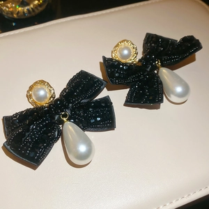 Detailed view of elegant bow earrings with white waterdrop pearls and gold metal edging