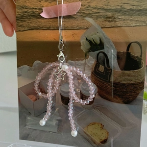 Close-up of pink beaded bow phone charm with silver star and white pearls on beach background