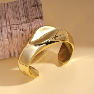 Detailed close-up of a wide irregular wavy golden cuff bracelet on a warm beige background