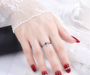 Close-up of a silver crescent ring with blue gemstone on hand with red manicure