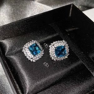 Detailed shot of luxury silver stud earrings with square blue gems and diamond accents in a box
