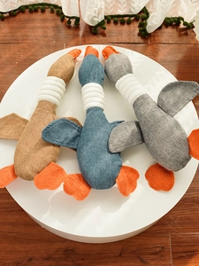 Three durable plush goose pet toys in brown, blue and grey displayed on a platform
