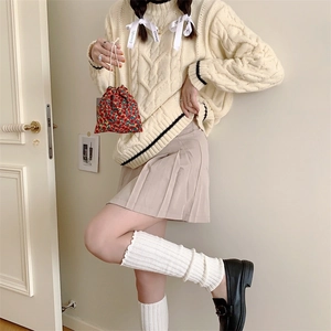 Detail of a red floral drawstring pouch paired with a cream cable knit sweater and skirt