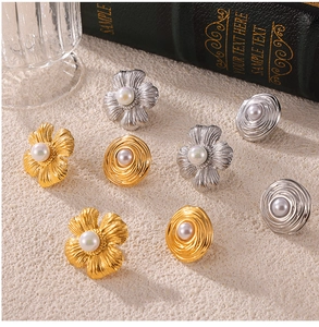 Detail of floral and swirl pearl earrings in gold and silver plating on textured surface