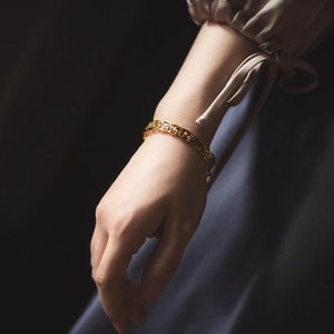 Macro shot of gold-plated open bangle with intricate retro hollow floral pattern